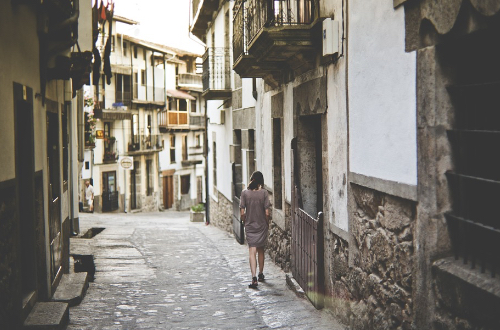 Kobieta spacerująca wąską uliczką miasteczka.