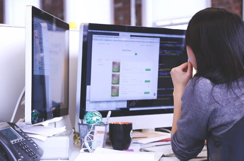 A woman working with two monitors.