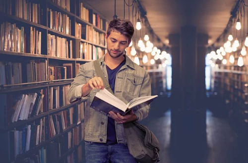 A man is reading a book between the shelves in the library.