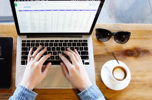 Woman working on the computer. There is a coffee cup and glasses on the table.