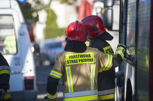 Dwóch strażaków stojących przy wozie w czasie akcji przeciwpożarowej.