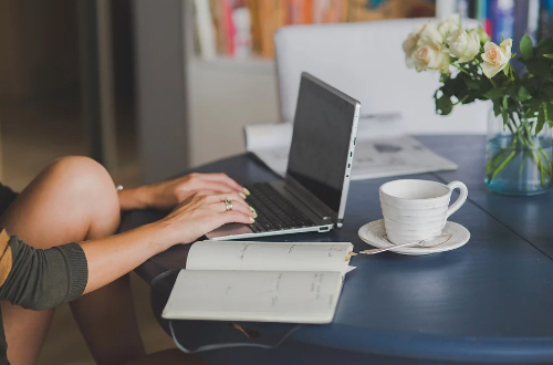 Woman working on the computer. There is a mug and notebook on the table.