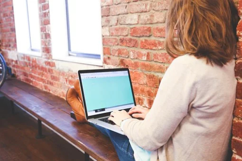 A woman sitting on a bench with a computer in her lap.